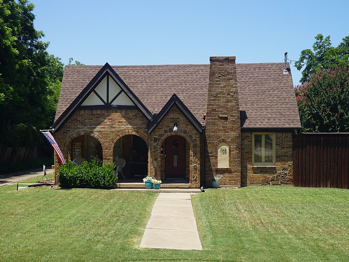 A Texas brick and stone house with a red tile roof and a mown lawn behind a low iron fence &mdash; representative imagery, not a specific Texas Pride job