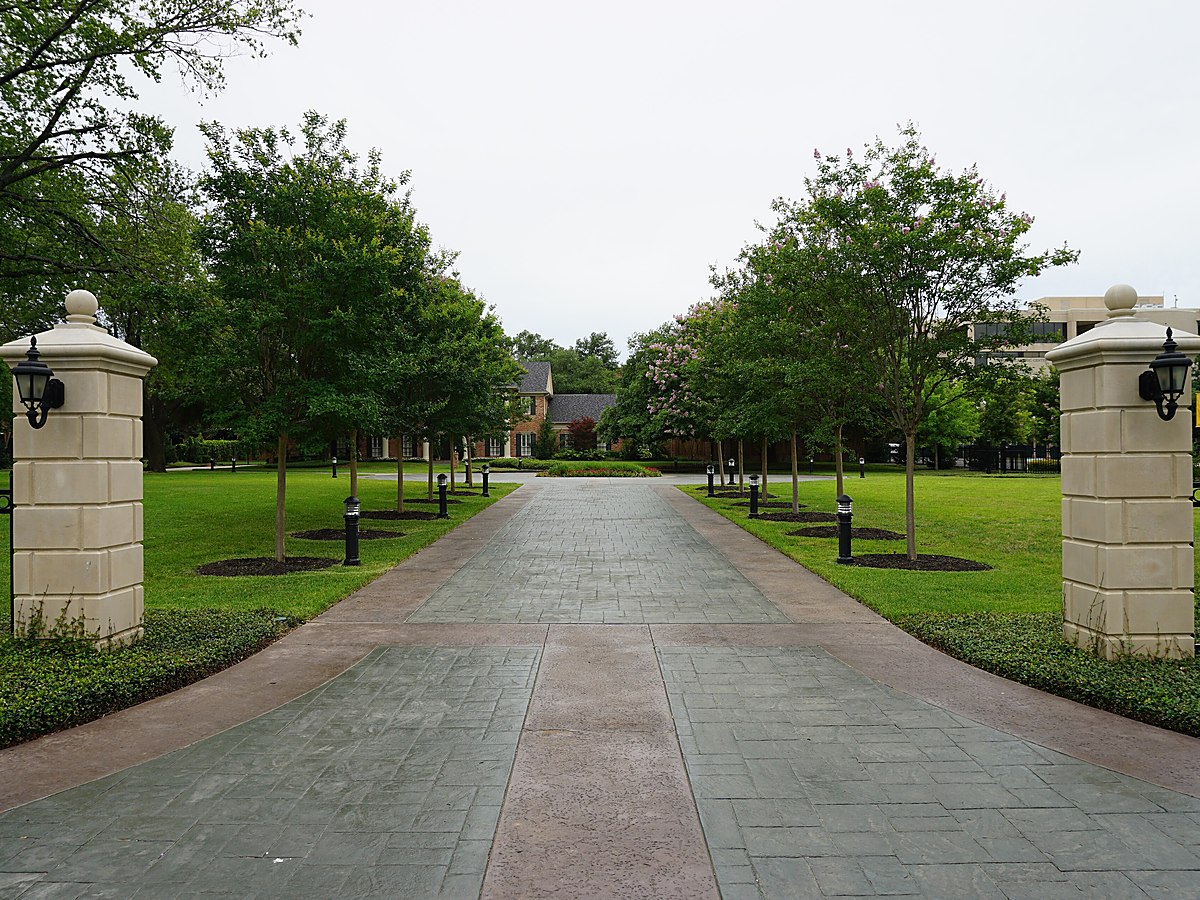 A landscaped entrance drive with stone gate posts leading into a wooded residential property &mdash; representative imagery, not a specific Texas Pride job