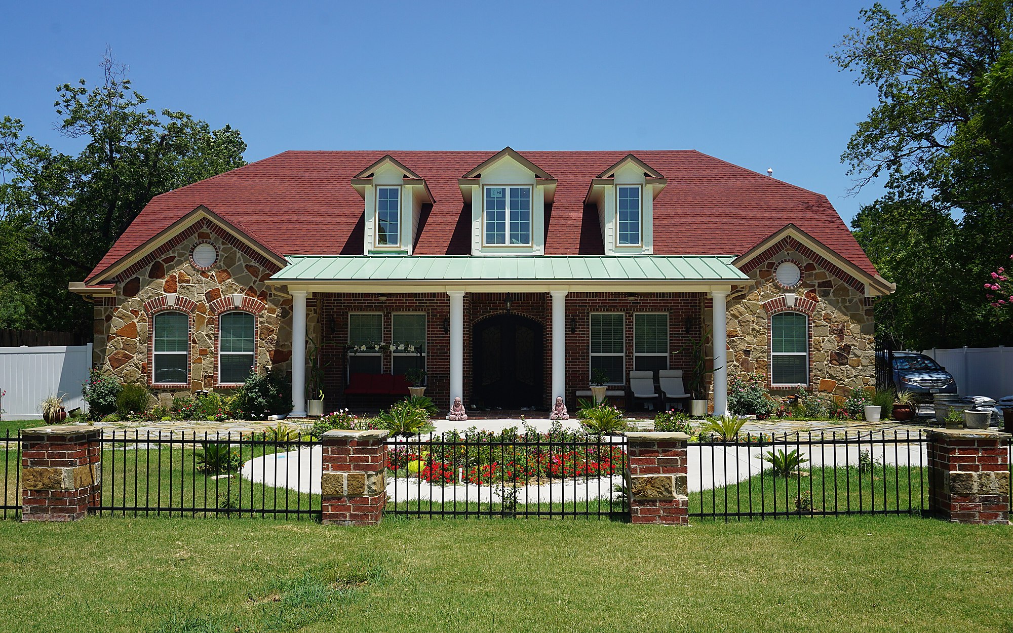 A Texas brick and stone house with a red tile roof, a deep covered porch and a mown lawn behind a low iron fence &mdash; representative imagery, not a specific Texas Pride job